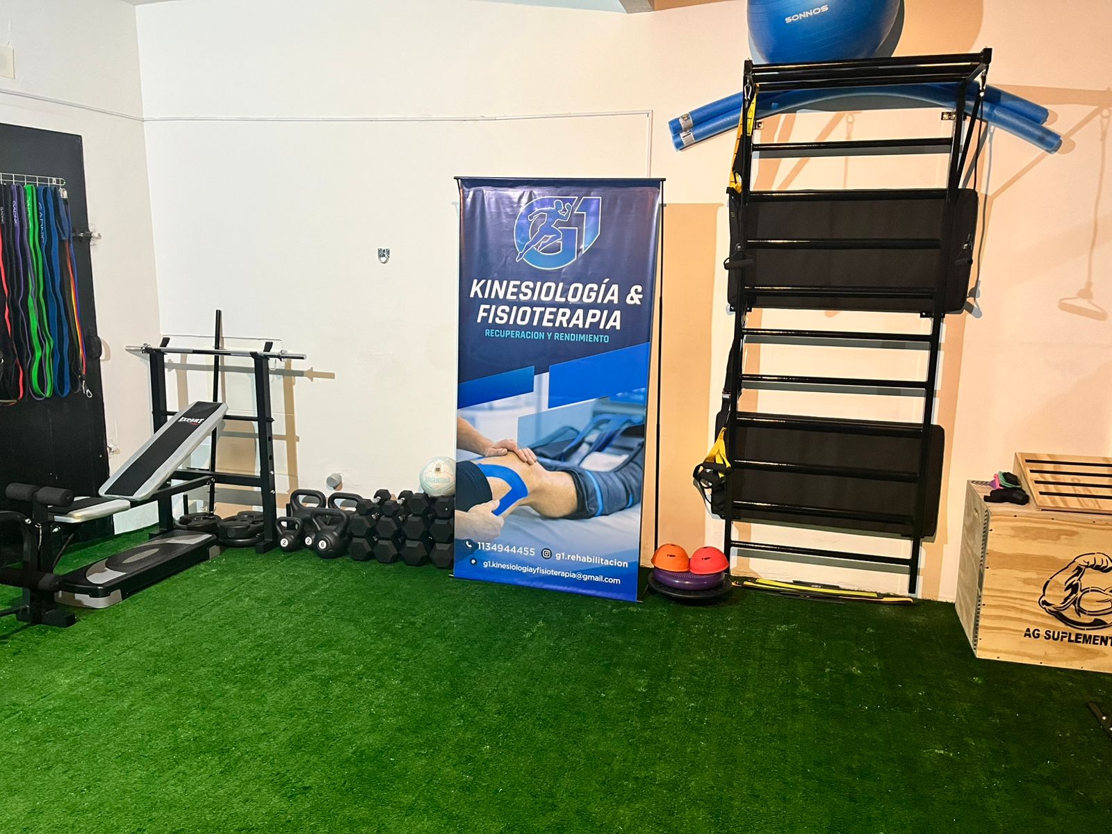 Modern physical therapy and sports recovery training room showing gym equipment, exercise balls, foam rollers, agility ladder on green artificial grass turf, pristine clean clinic background with natural light, professional sports rehabilitation clinic.